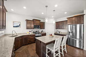 Kitchen featuring sink, hanging light fixtures, stainless steel appliances, dark hardwood / wood-style floors, and light stone counters