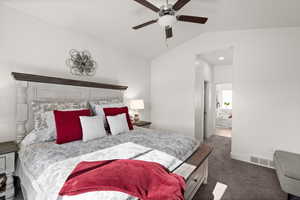 Bedroom featuring lofted ceiling, dark carpet, ensuite bath, and ceiling fan