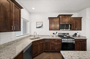 Kitchen featuring sink, dark wood-type flooring, stainless steel appliances, dark brown cabinetry, and light stone countertops