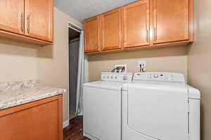 Washroom featuring a textured ceiling, dark wood-type flooring, cabinet space, and washer and dryer