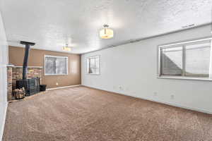 Unfurnished living room featuring   a wood stove, a textured ceiling, and carpet flooring