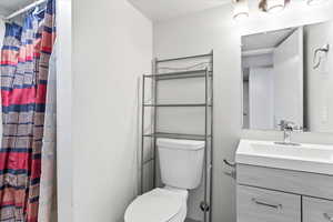 Bathroom with toilet, a shower with shower curtain, and vanity