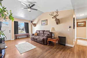 Living area with a ceiling fan, vaulted ceiling, a textured ceiling, wood finished floors, and baseboards