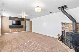 Unfurnished living room featuring, a wood stove, a textured ceiling, and carpet floors