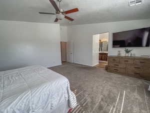 Bedroom with ceiling fan, ensuite bath, a textured ceiling, and carpet flooring