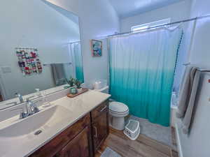 Full bathroom featuring wood-type flooring, toilet, shower / tub combo with curtain, and vanity