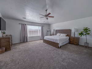 Bedroom featuring ceiling fan, vaulted ceiling, carpet, and a textured ceiling