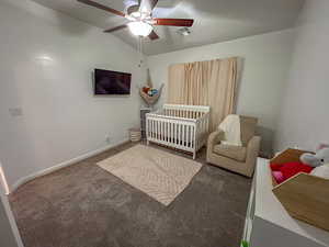 Carpeted bedroom with vaulted ceiling, a nursery area, and ceiling fan