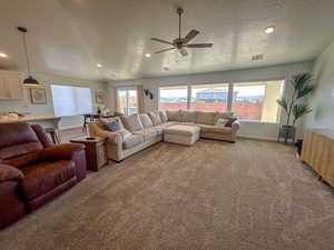 Carpeted living room with ceiling fan, a wealth of natural light, and a textured ceiling