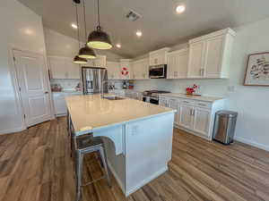 Kitchen featuring sink, white cabinetry, appliances with stainless steel finishes, pendant lighting, and a kitchen island with sink