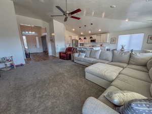 Living room with ceiling fan, dark carpet, vaulted ceiling, and a textured ceiling