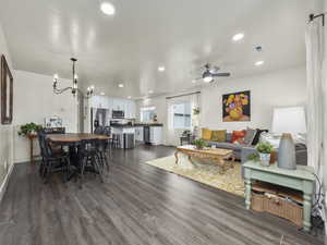 Living room kitchen, dining area with a notable chandelier, ceiling fan, and dark hardwood / wood-style floors