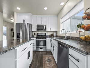 Kitchen featuring dark hardwood / wood-style floors, white cabinetry, sink, dark stone countertops, and stainless steel appliances