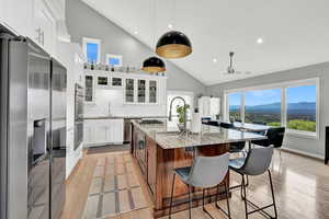 Kitchen with appliances with stainless steel finishes, white cabinets, light stone counters, a mountain view, and a center island with sink