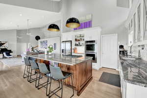 Kitchen with a large island with sink, white cabinets, light stone counters, and stainless steel appliances