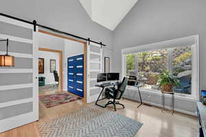 Office space featuring hardwood / wood-style floors, high vaulted ceiling, and a barn door