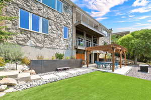 Back of house featuring a balcony, a pergola, a patio area, and a lawn