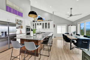 Kitchen featuring a breakfast bar area, stone counters, white cabinetry, appliances with stainless steel finishes, and decorative light fixtures