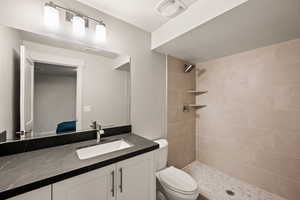 Bathroom featuring tiled shower, vanity, and toilet