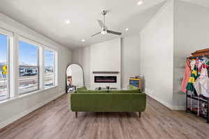 Living room with ceiling fan, a large fireplace, vaulted ceiling, and light hardwood / wood-style flooring