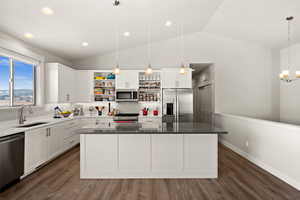 Kitchen with lofted ceiling, appliances with stainless steel finishes, hanging light fixtures, white cabinets, and a kitchen island