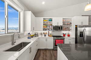 Kitchen with sink, white cabinetry, vaulted ceiling, appliances with stainless steel finishes, and pendant lighting