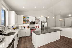 Kitchen with a kitchen island, sink, white cabinets, hanging light fixtures, and stainless steel appliances