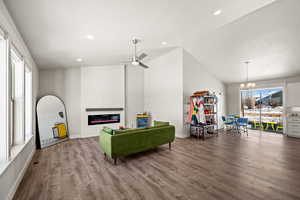 Living room with lofted ceiling, hardwood / wood-style flooring, a fireplace, and ceiling fan with notable chandelier