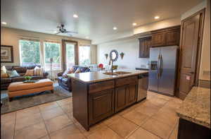 Kitchen featuring light tile patterned flooring, appliances with stainless steel finishes, a kitchen island with sink, and dark brown cabinets