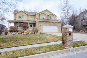 View of property with a garage, covered porch, and a front lawn