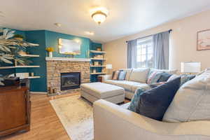 Living room featuring a stone fireplace, a textured ceiling, and light hardwood / wood-style floors