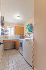 Laundry area featuring cabinets, light tile patterned floors, a textured ceiling, and independent washer and dryer