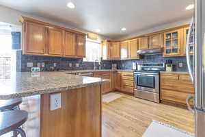 Kitchen featuring a breakfast bar area, light stone counters, light wood-type flooring, appliances with stainless steel finishes, and kitchen peninsula