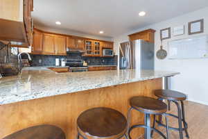 Kitchen featuring sink, appliances with stainless steel finishes, light stone countertops, decorative backsplash, and kitchen peninsula