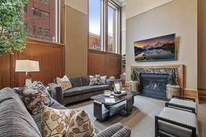 Living room with carpet flooring, a high ceiling, wood walls, and a high end fireplace