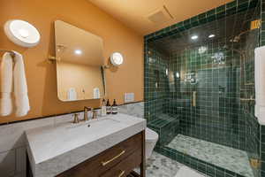 Bathroom featuring vanity, a shower with shower door, toilet, and tile walls