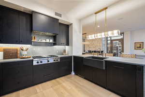 Kitchen with sink, hanging light fixtures, stainless steel gas stovetop, light hardwood / wood-style floors, and backsplash