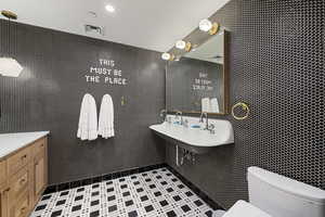 Bathroom featuring vanity, toilet, and tile walls