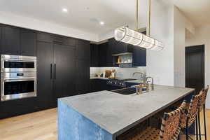 Kitchen with sink, decorative light fixtures, a kitchen breakfast bar, stainless steel double oven, and light hardwood / wood-style floors