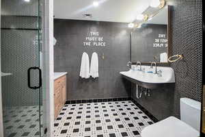 Bathroom featuring tile walls, sink, a shower with shower door, and toilet