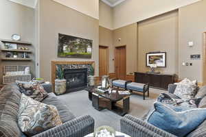 Carpeted living room featuring crown molding, a high end fireplace, and a towering ceiling