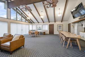 Interior space with ceiling fan with notable chandelier, high vaulted ceiling, beamed ceiling, and carpet