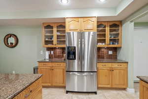 Kitchen with light tile patterned floors, decorative backsplash, dark stone counters, and stainless steel refrigerator with ice dispenser