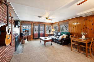 Appt. Basement Carpeted living room featuring wooden walls, a fireplace, french doors, and ceiling fan