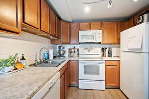 Appt. Kitchen featuring tasteful backsplash, sink, white appliances, and light hardwood / wood-style floors