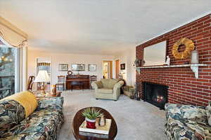 Living room with a brick fireplace, carpet floors, and a textured ceiling