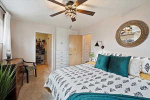 Carpeted bedroom with ceiling fan and a textured ceiling