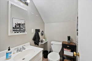 Bathroom featuring lofted ceiling, toilet, vanity, and a textured ceiling