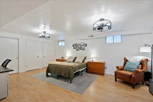 Appt. Bedroom with multiple closets, a notable chandelier, light hardwood / wood-style flooring, and a textured ceiling