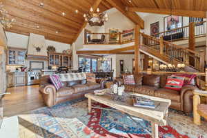 Living room with an inviting chandelier, high vaulted ceiling, wood ceiling, and light hardwood / wood-style floors